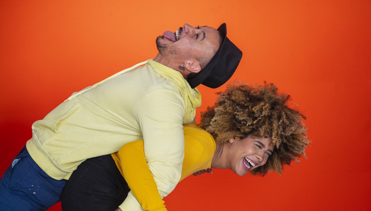 Happy couple playing and messing in front of orange background.