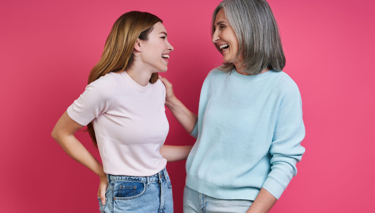 Happy mother and adult daughter looking at each other against pink background