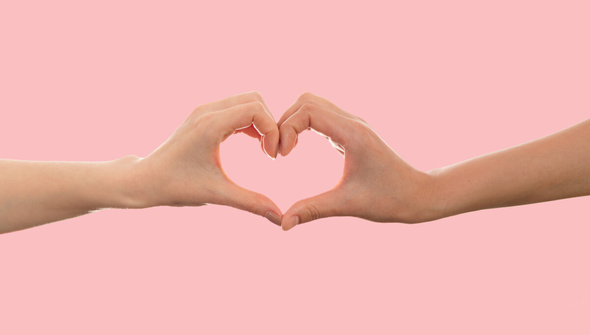 Two hands in heart shape in front of pink background