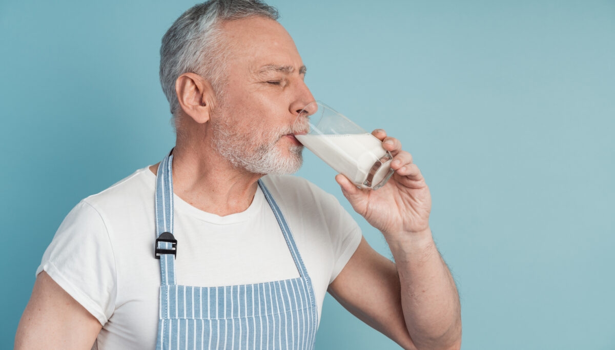 Side view, senior man drinking milk, closing his eyes. Isolated on blue background, copy space, place for text.