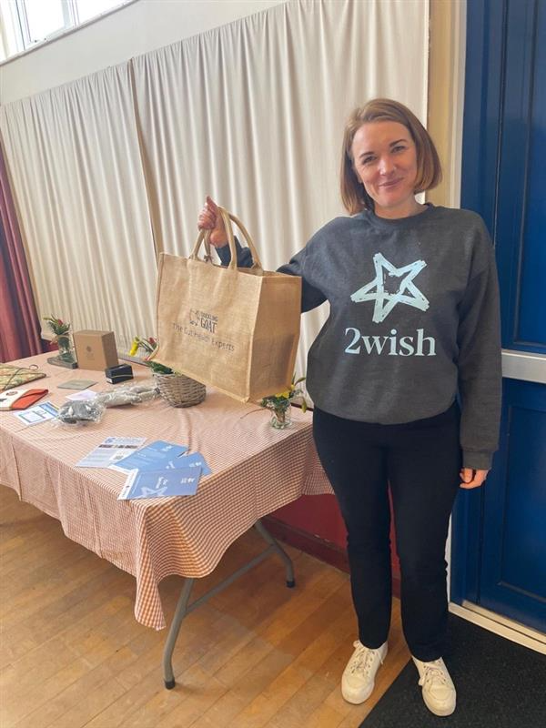 Image of Charity Worker at 2wish Cymru, smiling wearing 2wish jumper and holding Chuckling Goat bag.