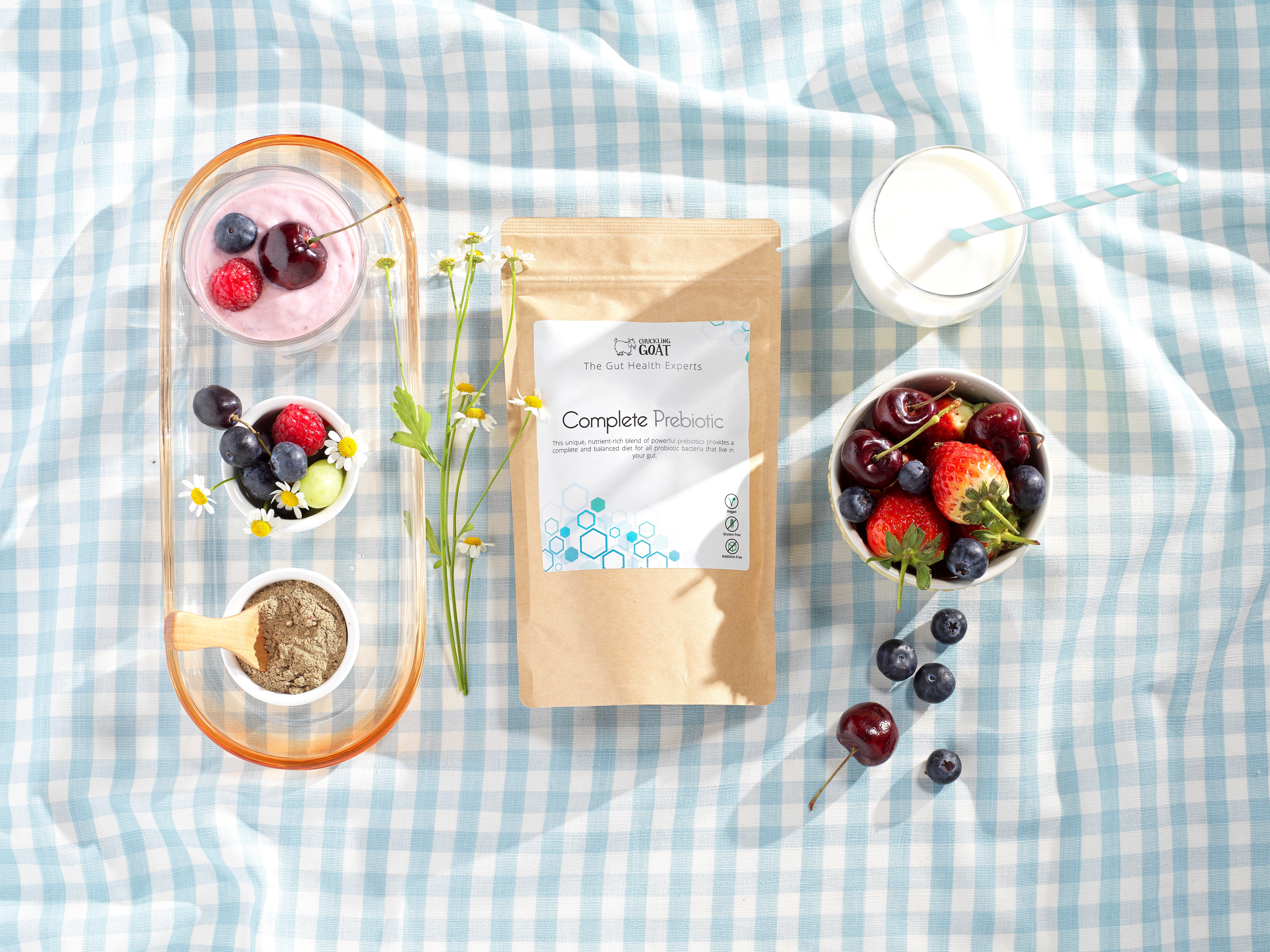 Image of Chuckling Goat Complete Prebiotic on blue and white picnic blanket among different fruits.