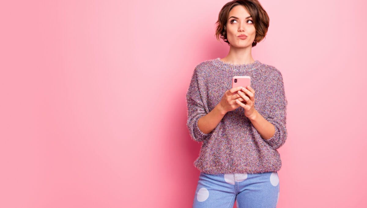 Portrait of woman using mobile phone isolated over pink pastel colour background