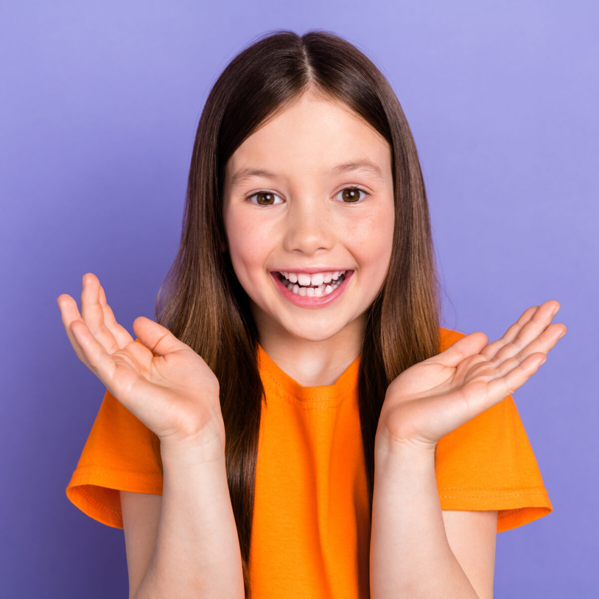 Portrait of young girl preschool age clapping arms positive orange t shirt hooray entertainment day isolated on purple color background.