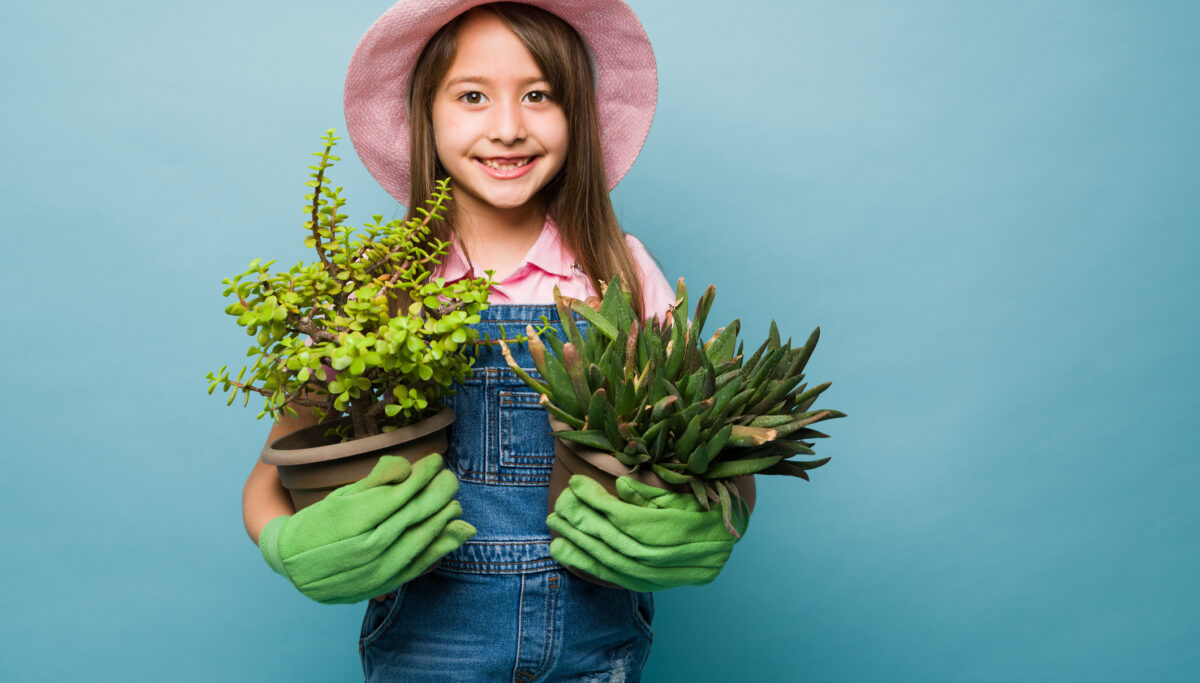 Girl smiling holding to plants in pots on a blue background.