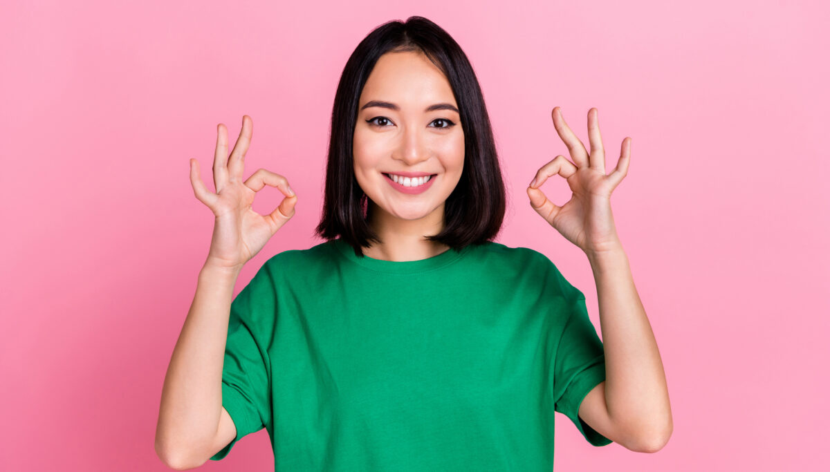 Happy woman showing OK gesture with her hands, on a pink background.