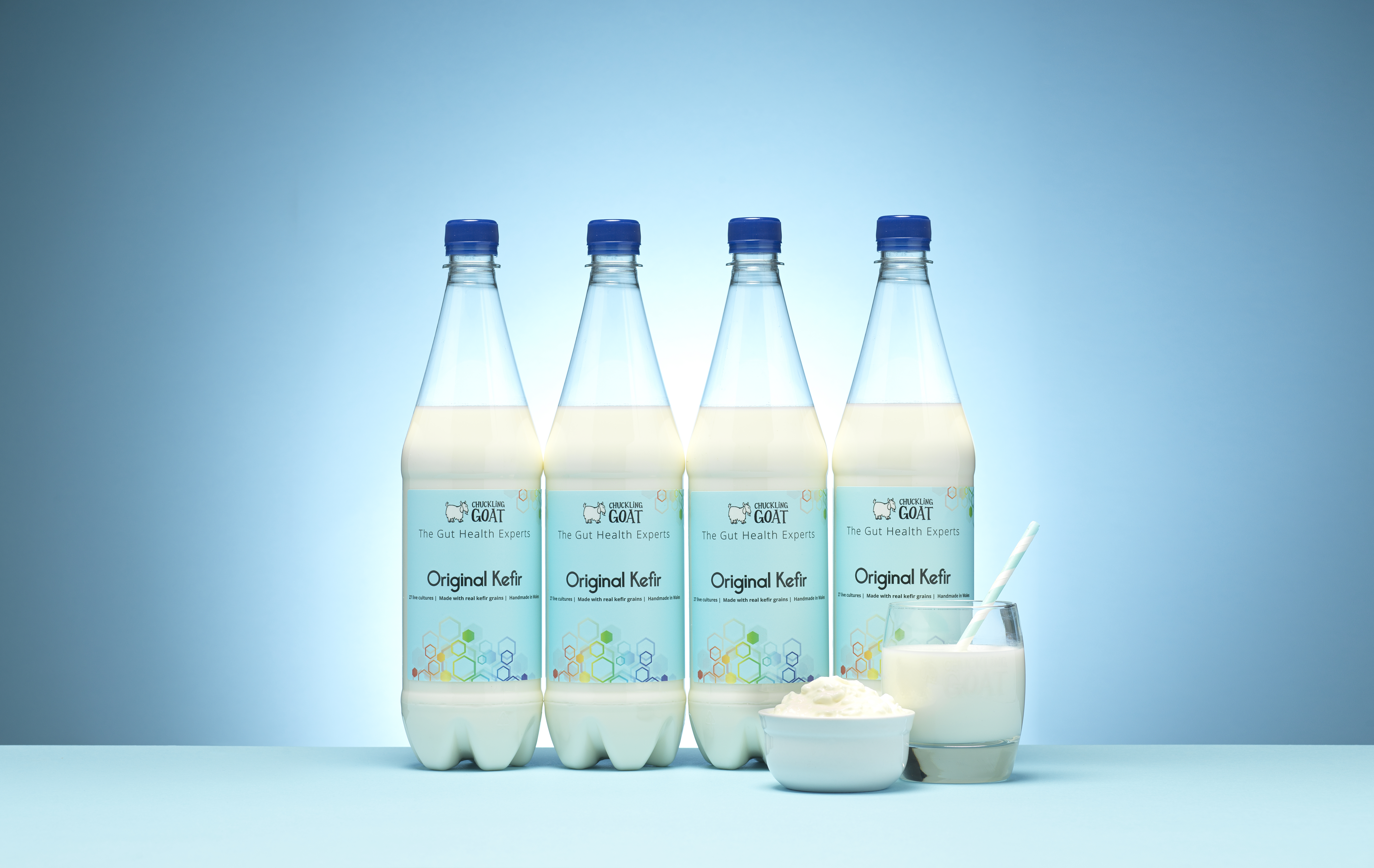 Four bottles of Chuckling Goat Original Kefir on a blue background.
