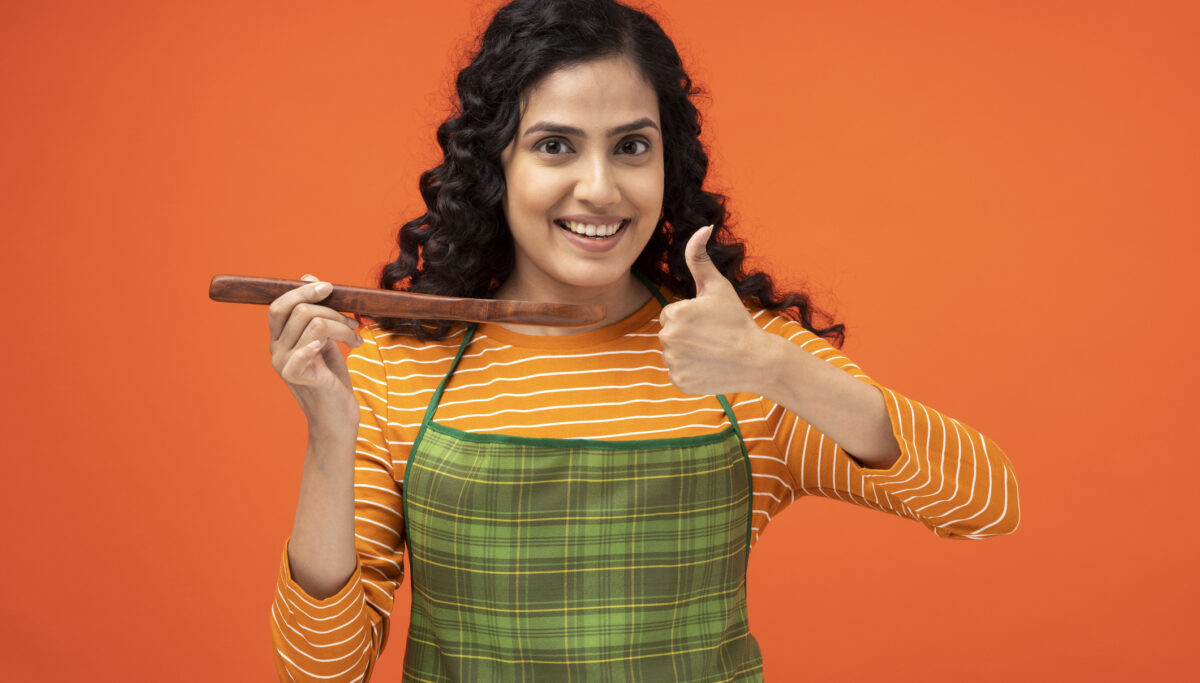 Young woman, Cooking, holding up spoon, orange background