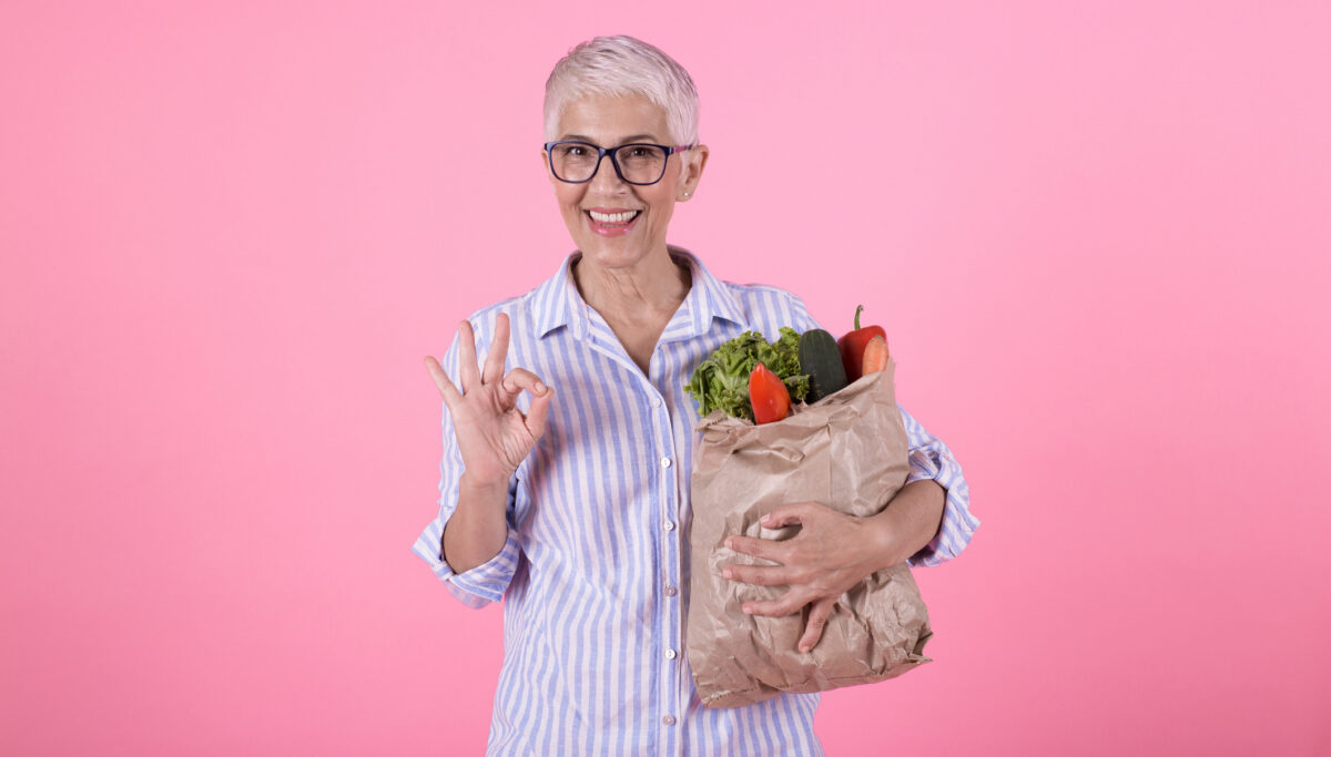 Studio portrait of a happy mature woman holding a bag of healthy groceries.