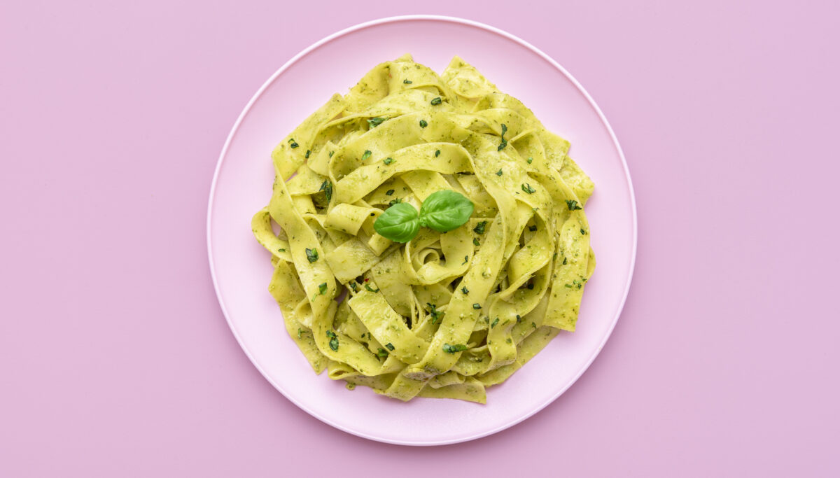 Plate of homemade pesto pasta on a pink background.