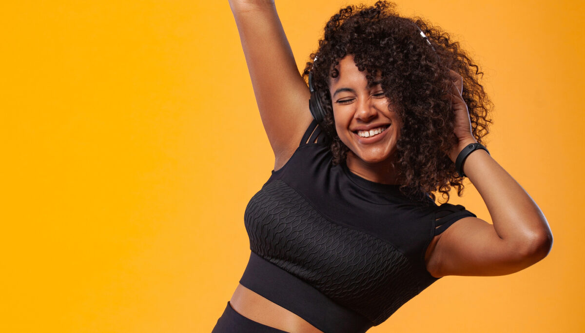 Lifestyle Concept - Portrait of beautiful African American woman joyful listening to music on mobile phone. Yellow pastel studio background.