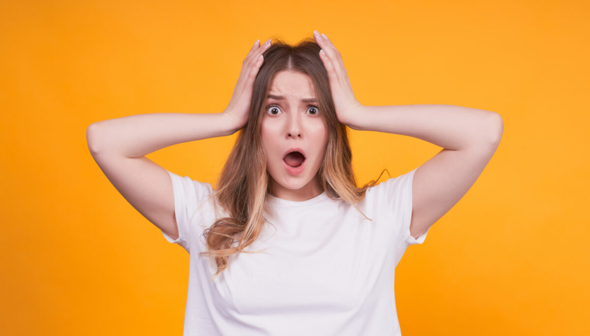 Portrait of an agitated and young girl holding her hands behind her head and lowering her jaw, shocked by the work, responsibilities that need to be addressed.