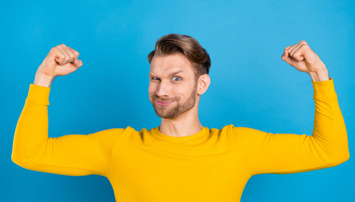 Photo of young guy happy positive smile show arms muscles bodybuilding isolated over blue color background