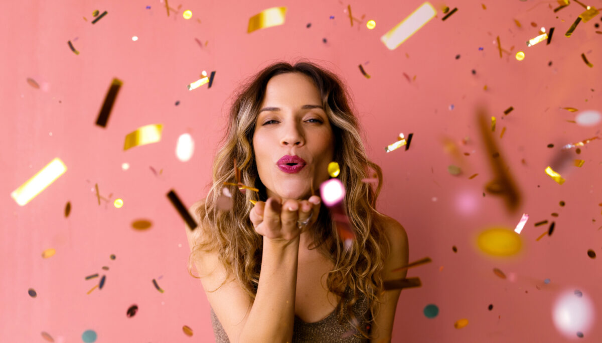 It's party time: A cheerful attractive female in glitter brown dress sending kisses while looking at camera. (studio shot, pink background)