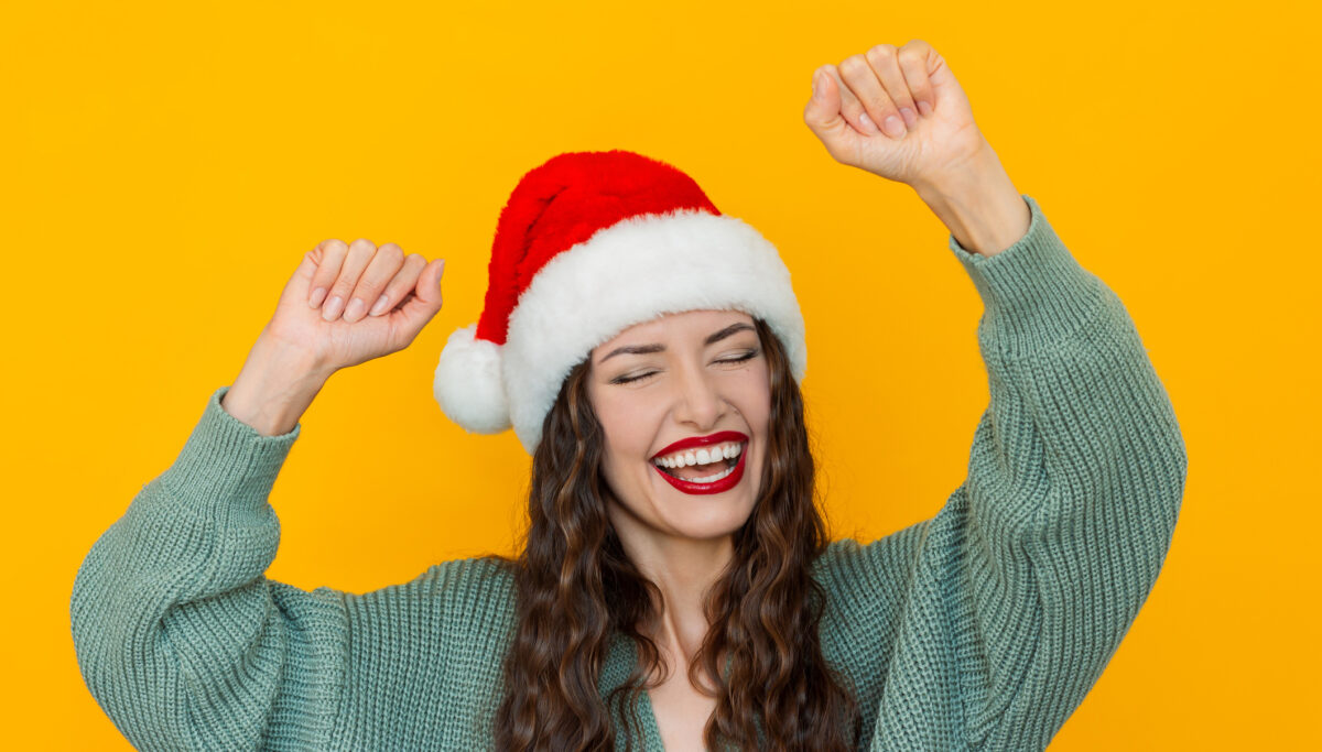 Happy woman dancing wearing a santa hat on a yellow background