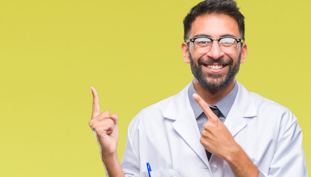 Adult scientist or doctor man wearing white coat over isolated background smiling and looking at the camera pointing with two hands and fingers to the side.