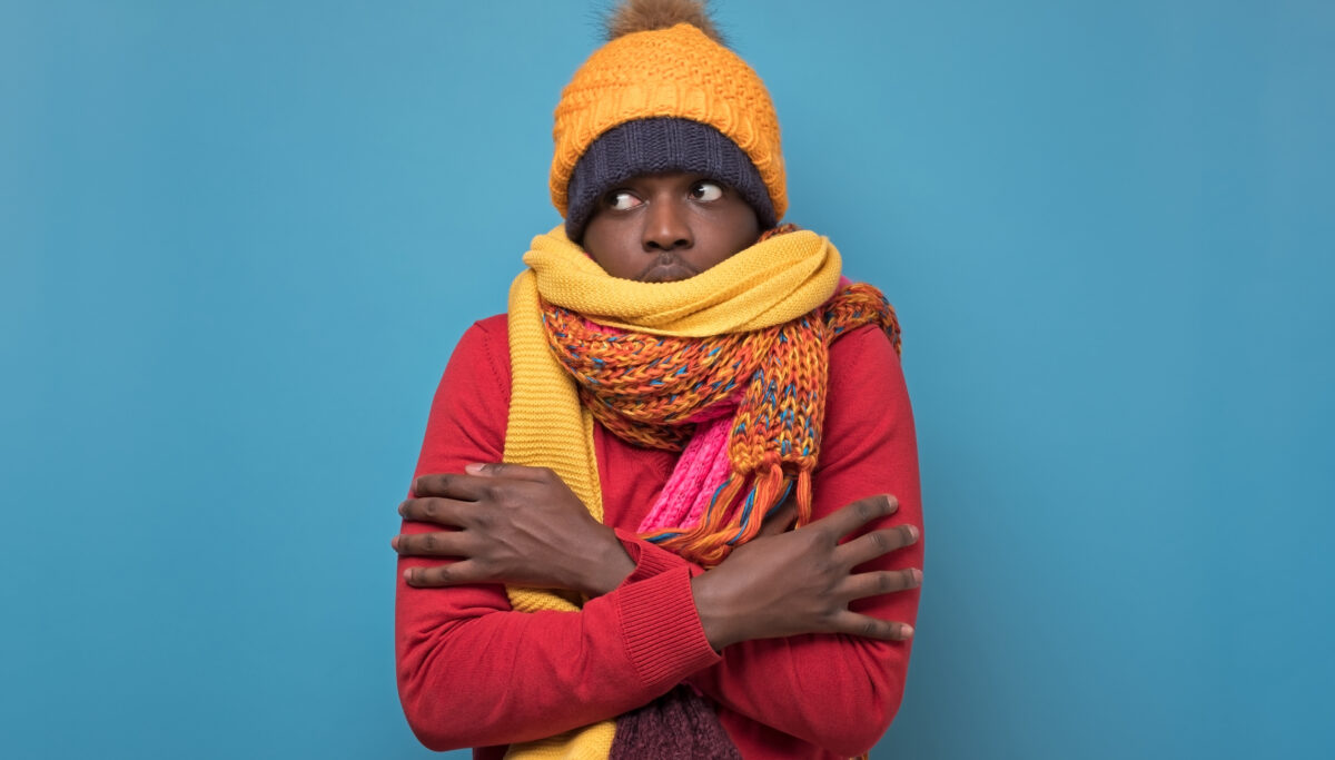 Man in several hats and scarfs on blue background. Winter fashion.