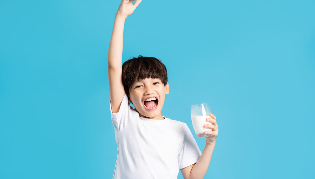 Portrait of boy holding cup of milk, isolated on blue background