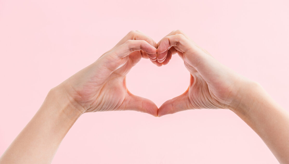 Woman hands making a heart shape on pink background