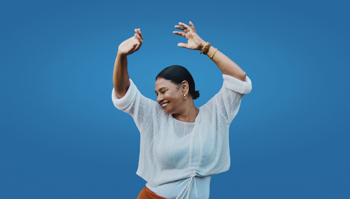 Smiling woman dances freely against a solid blue background, expressing authentic joy and movement