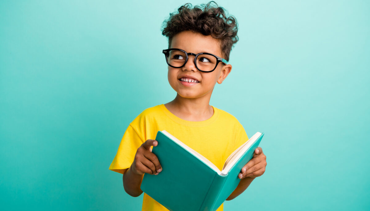 Photo of intelligent schoolboy with brown hair dressed yellow t-shirt holding book look empty space isolated on turquoise color background.