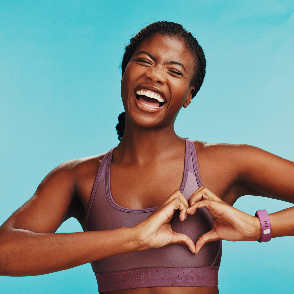Woman creating heart with hands, smiling, kindness, blue background