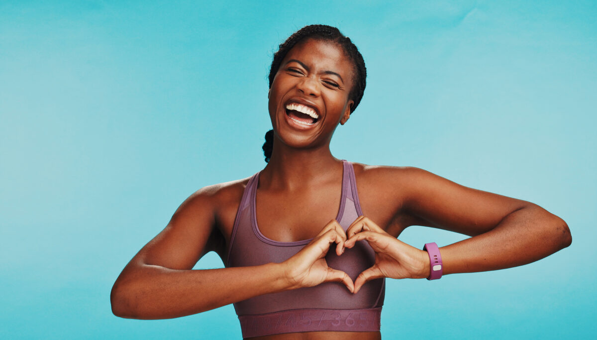Woman creating heart with hands, smiling, kindness, blue background