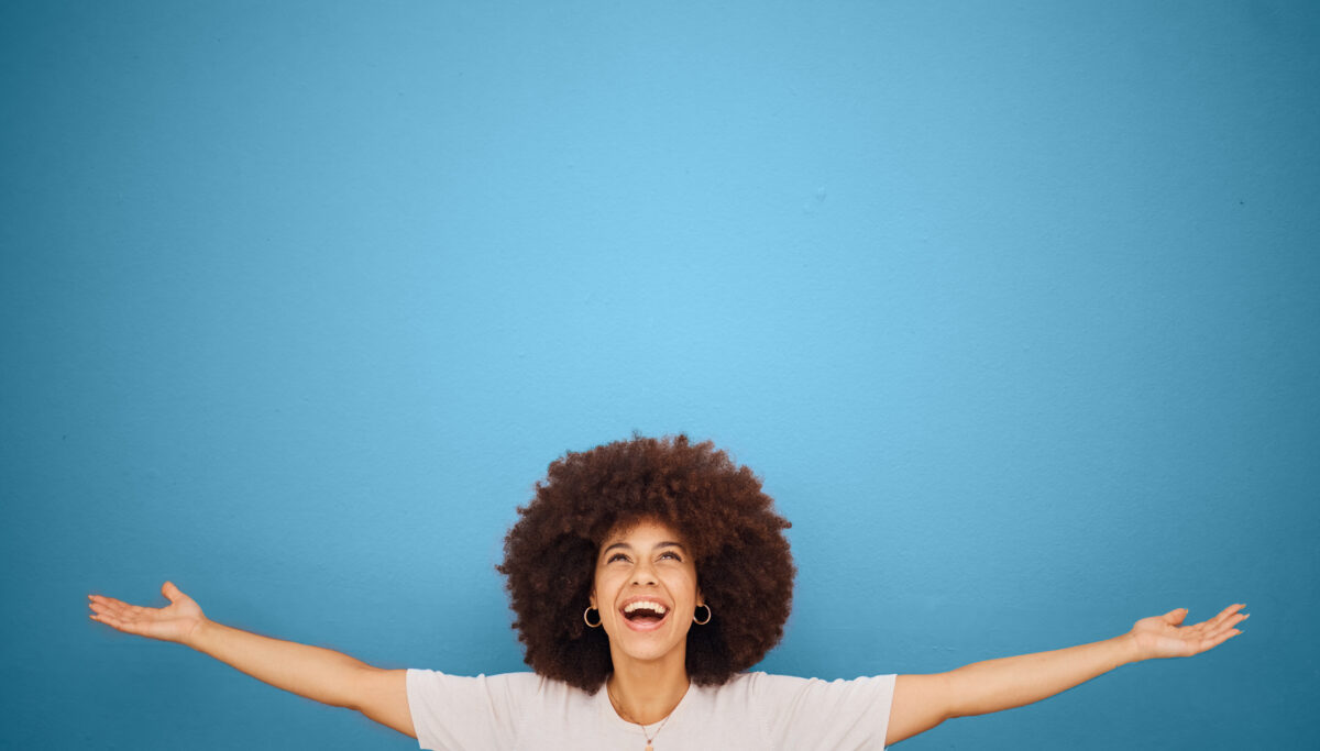 Woman celebrating, arms wide open, smiling, on isolated blue background, positivity