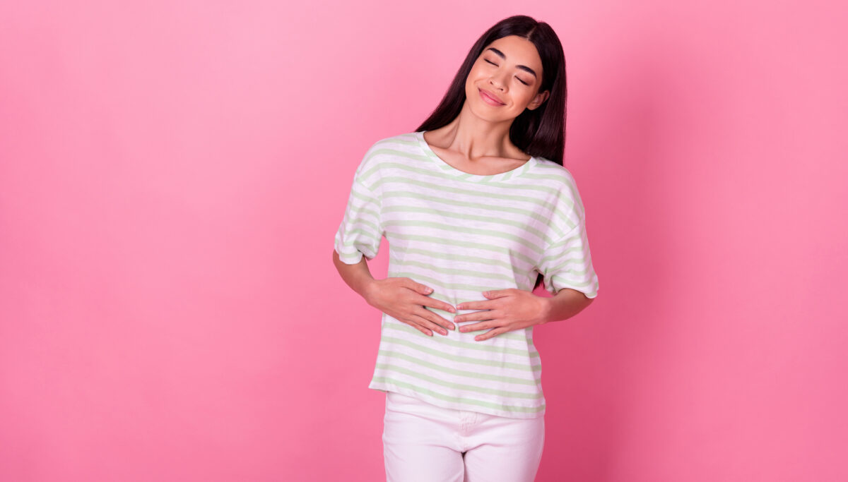 Photo of happy woman with hands on stomach, healthy on pink background