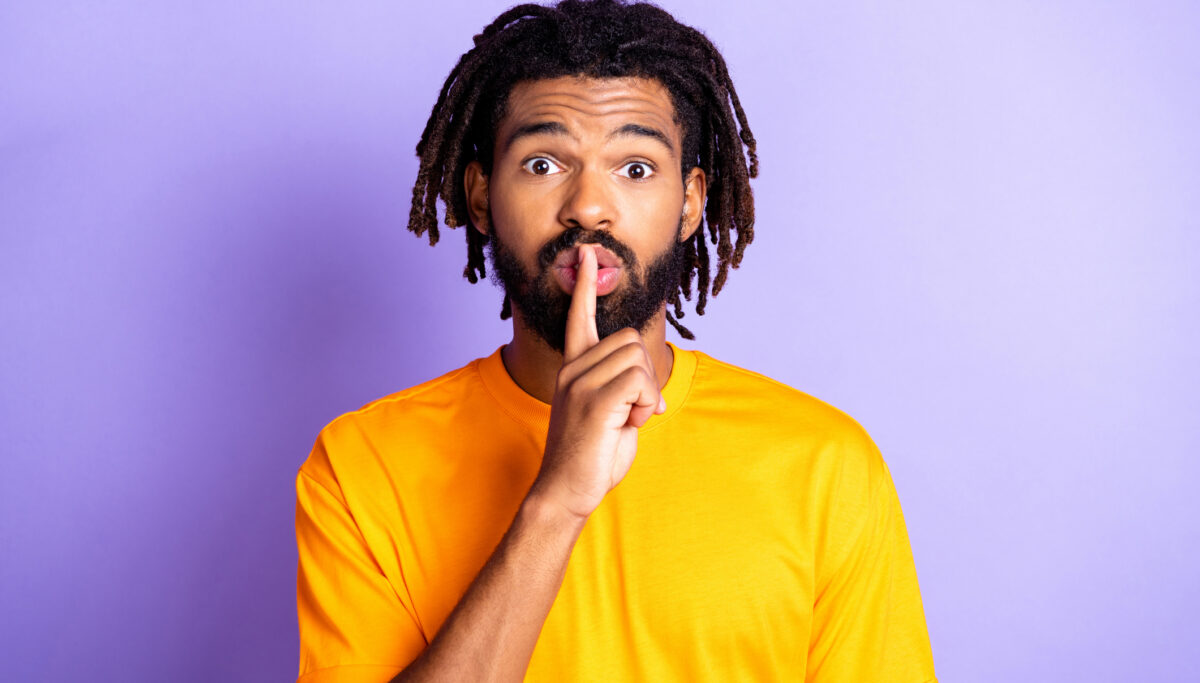 Man surprised, shushing, hand to mouth on purple background