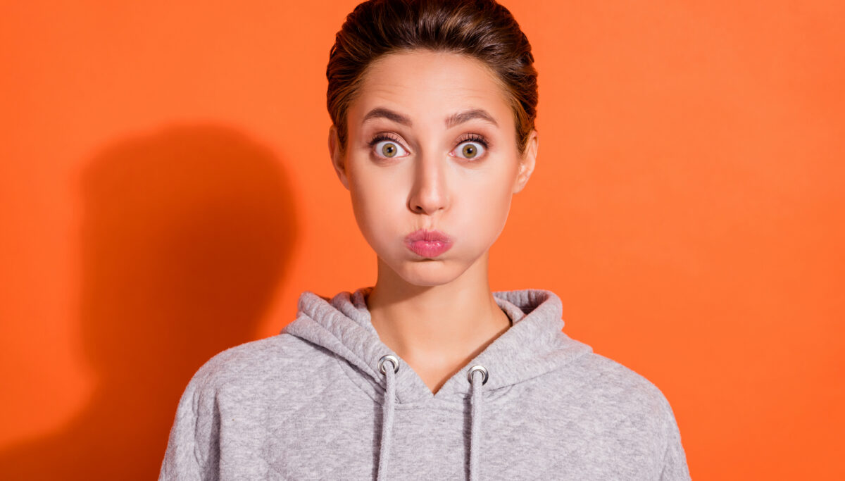 Young woman, bloated cheeks, surprised on solid orange background