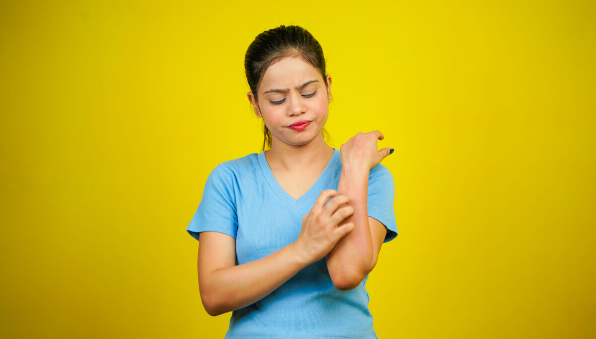 oung women have skin problems, irritation on her skin, skin infection itching red rash, arm scratching with hands, isolated over yellow background