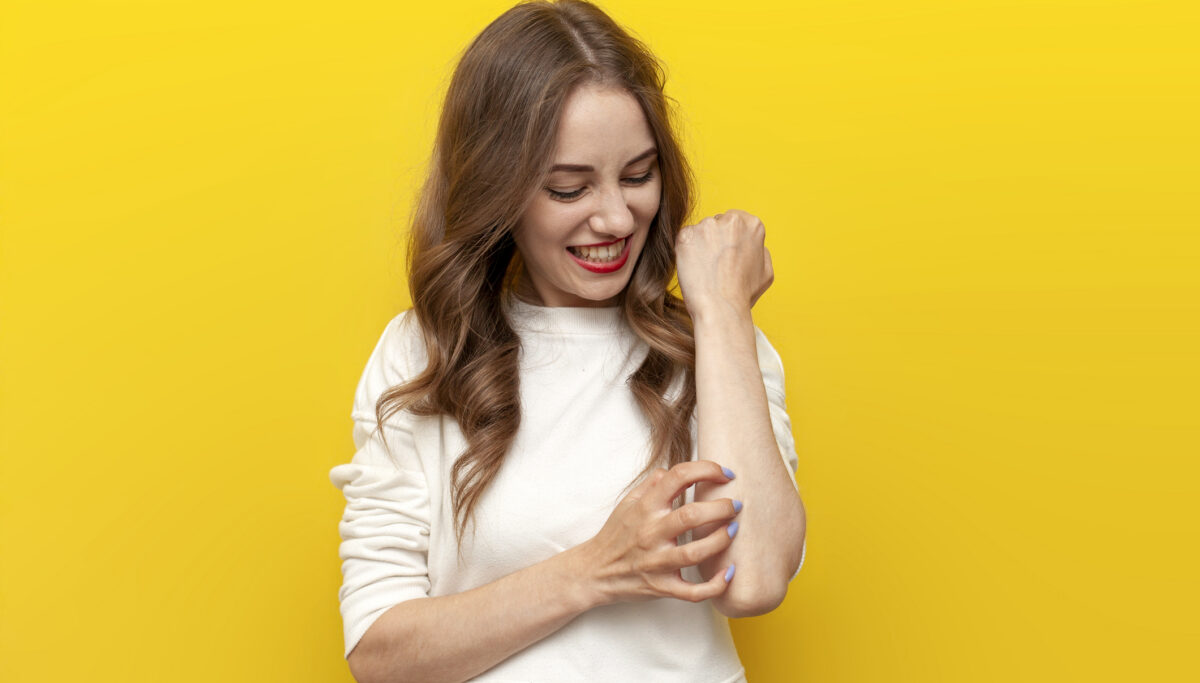 woman scratches her hand on yellow isolated background