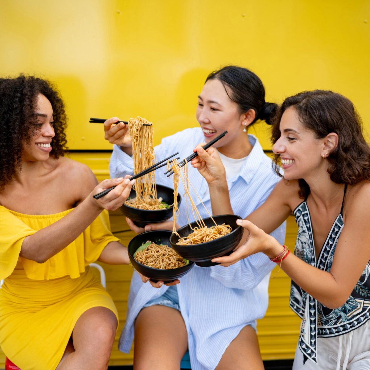 Group of female friends eating noodles together, smiling