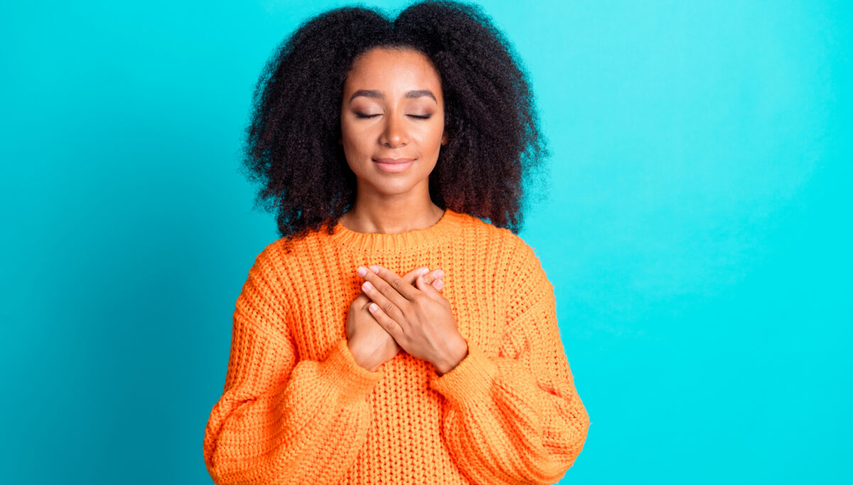 Photo of lovely young lady touch chest grateful closed eyes dressed stylish knitted orange garment isolated on aquamarine color background.