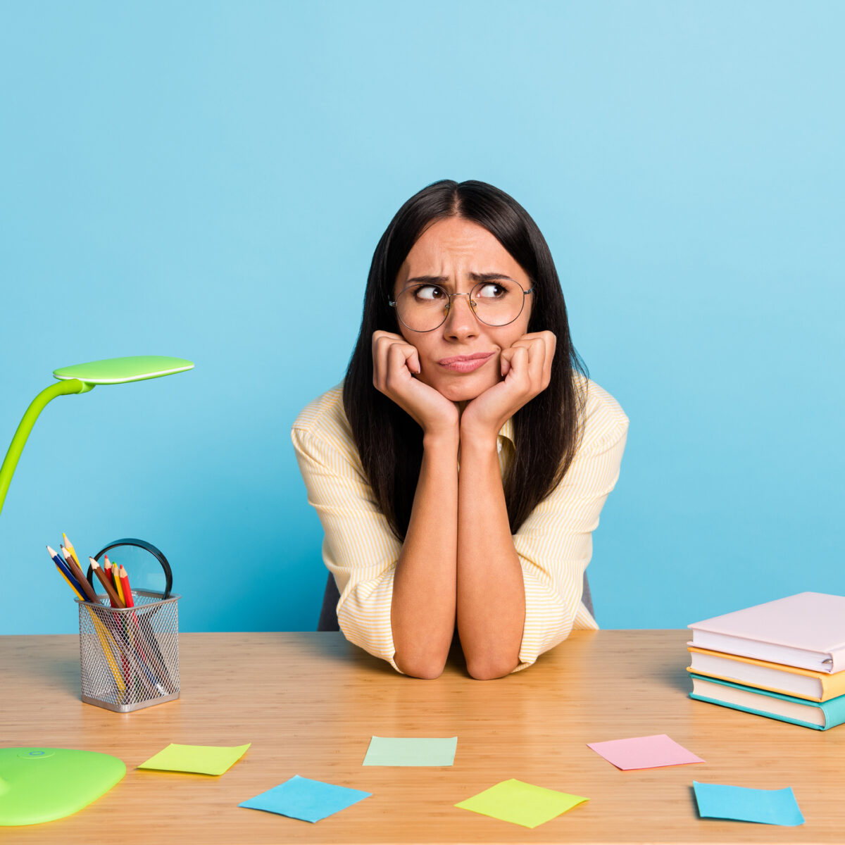 Photo of tired bored young businesswoman look empty space sit table bad mood isolated on pastel blue color background