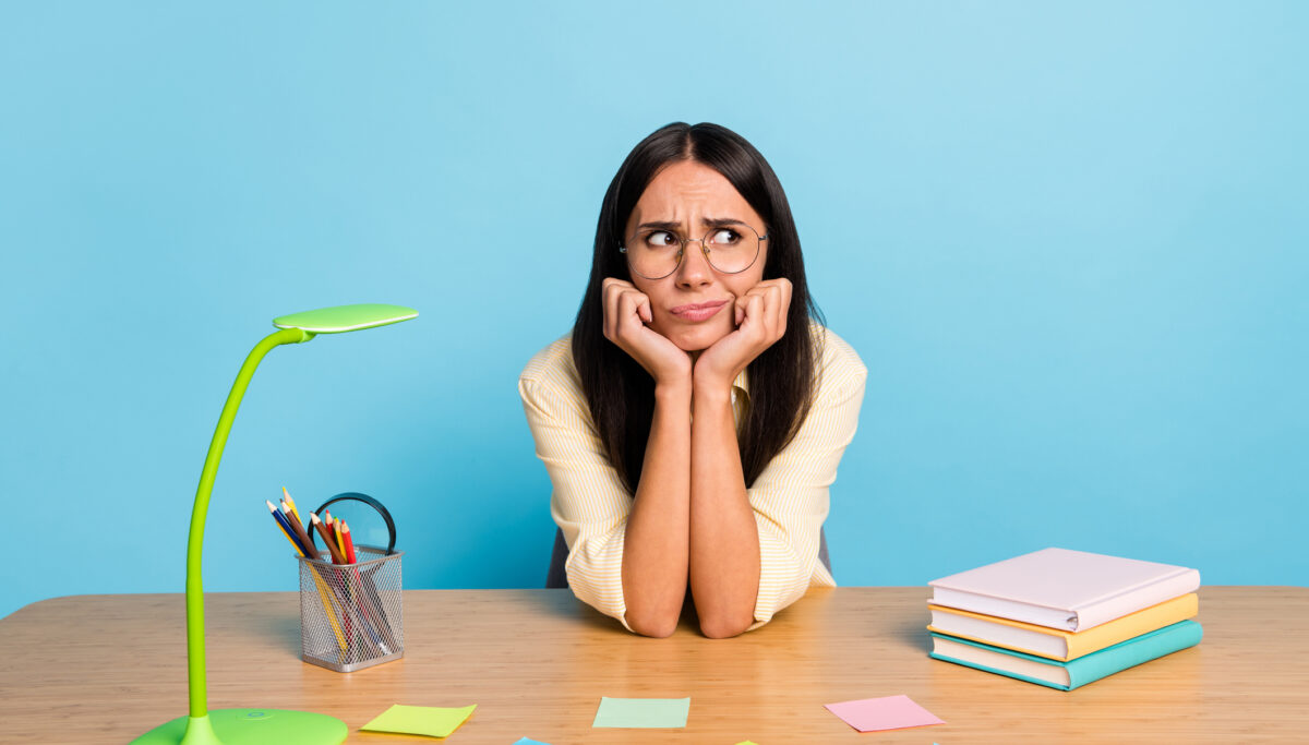 Photo of tired bored young businesswoman look empty space sit table bad mood isolated on pastel blue color background
