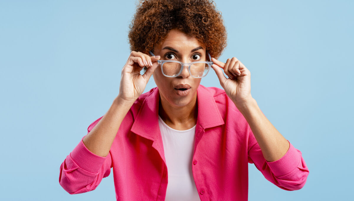 Woman with glasses showing astonishment and wide eyes, expressing disbelief on blue background