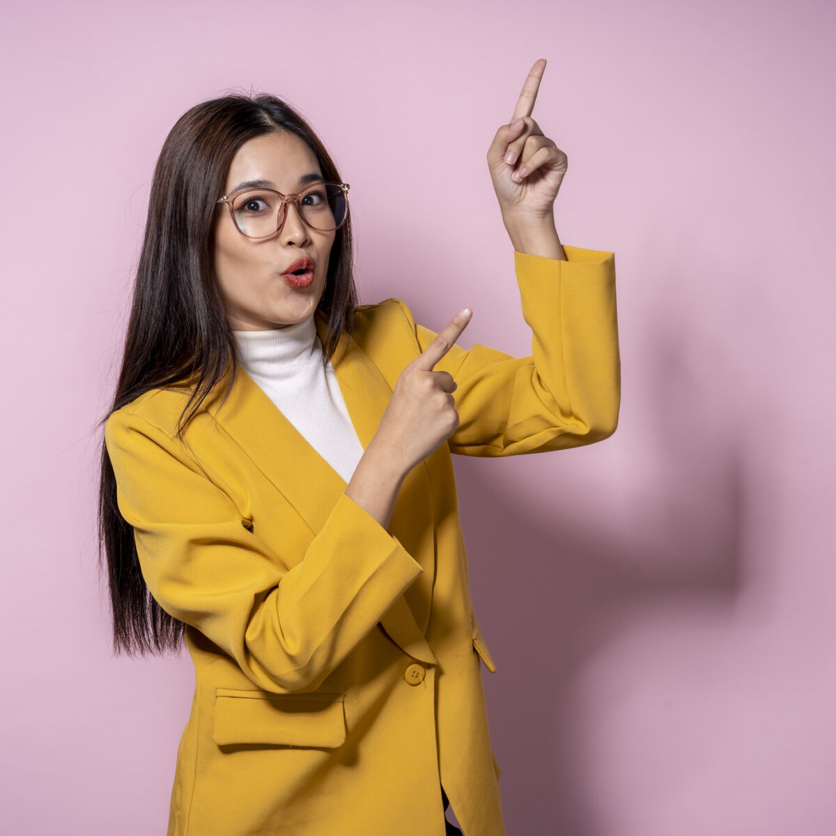 A woman in a yellow jacket pointing to something. She is wearing glasses and has a surprised look on her face