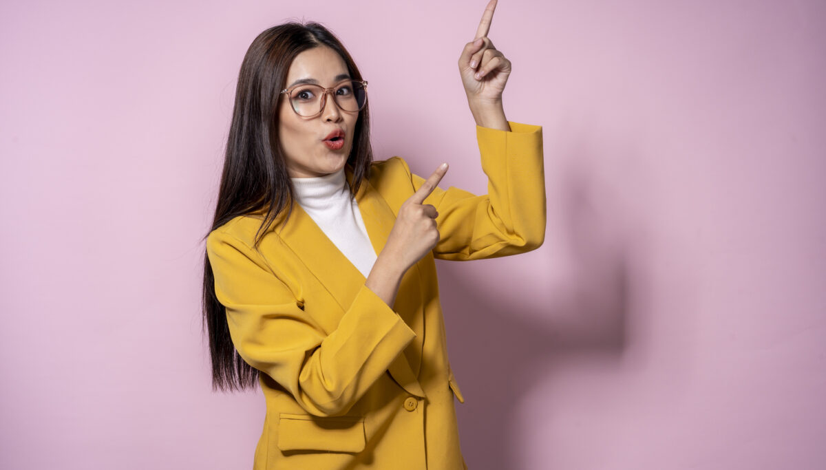 A woman in a yellow jacket pointing to something. She is wearing glasses and has a surprised look on her face
