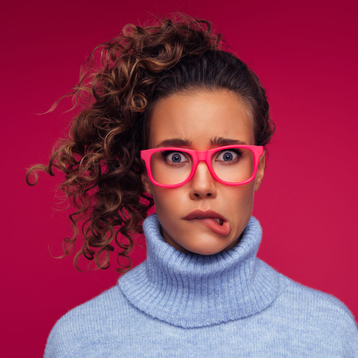 Woman with curly hair pulling funny, unsure face on dark pink background