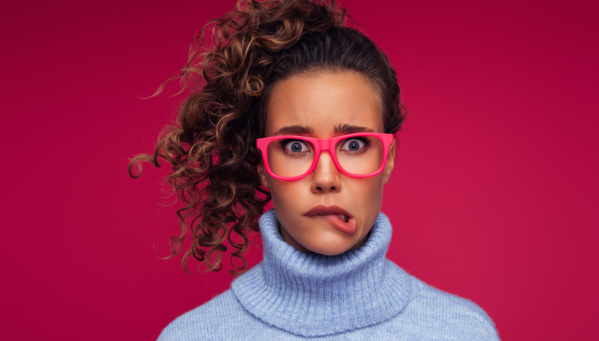 Woman with curly hair pulling funny, unsure face on dark pink background