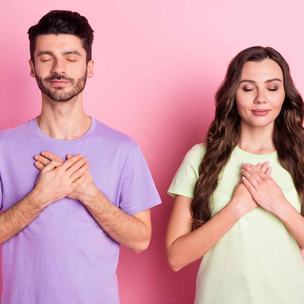 Portrait of attractive peaceful focused couple praying mental health heart isolated over pink pastel color background.