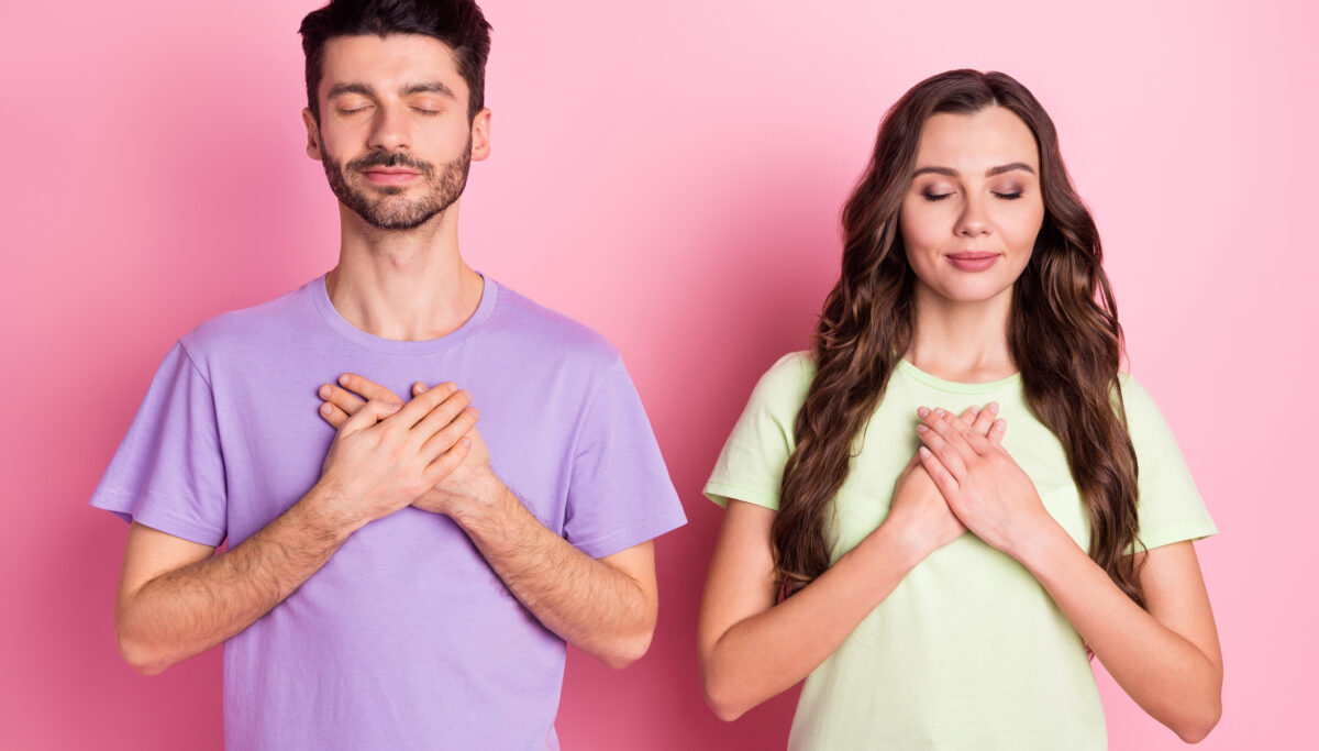 Portrait of attractive peaceful focused couple praying mental health heart isolated over pink pastel color background.