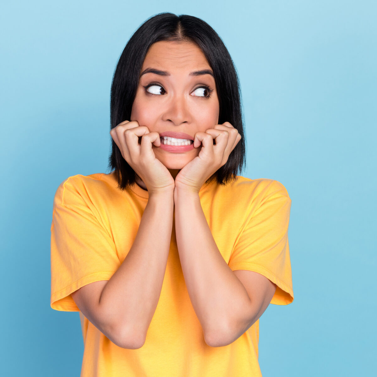 Photo of horrified scared cute woman with bob hairstyle wear yellow t-shirt look empty space bite hands isolated on blue color background.