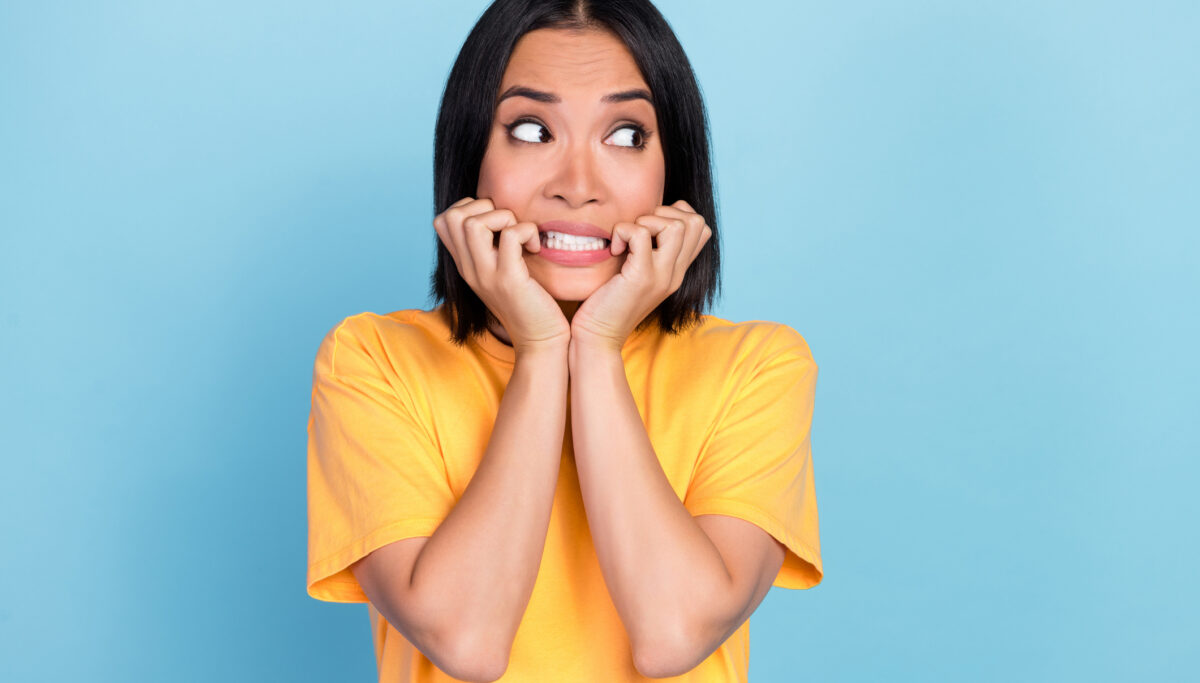 Photo of horrified scared cute woman with bob hairstyle wear yellow t-shirt look empty space bite hands isolated on blue color background.