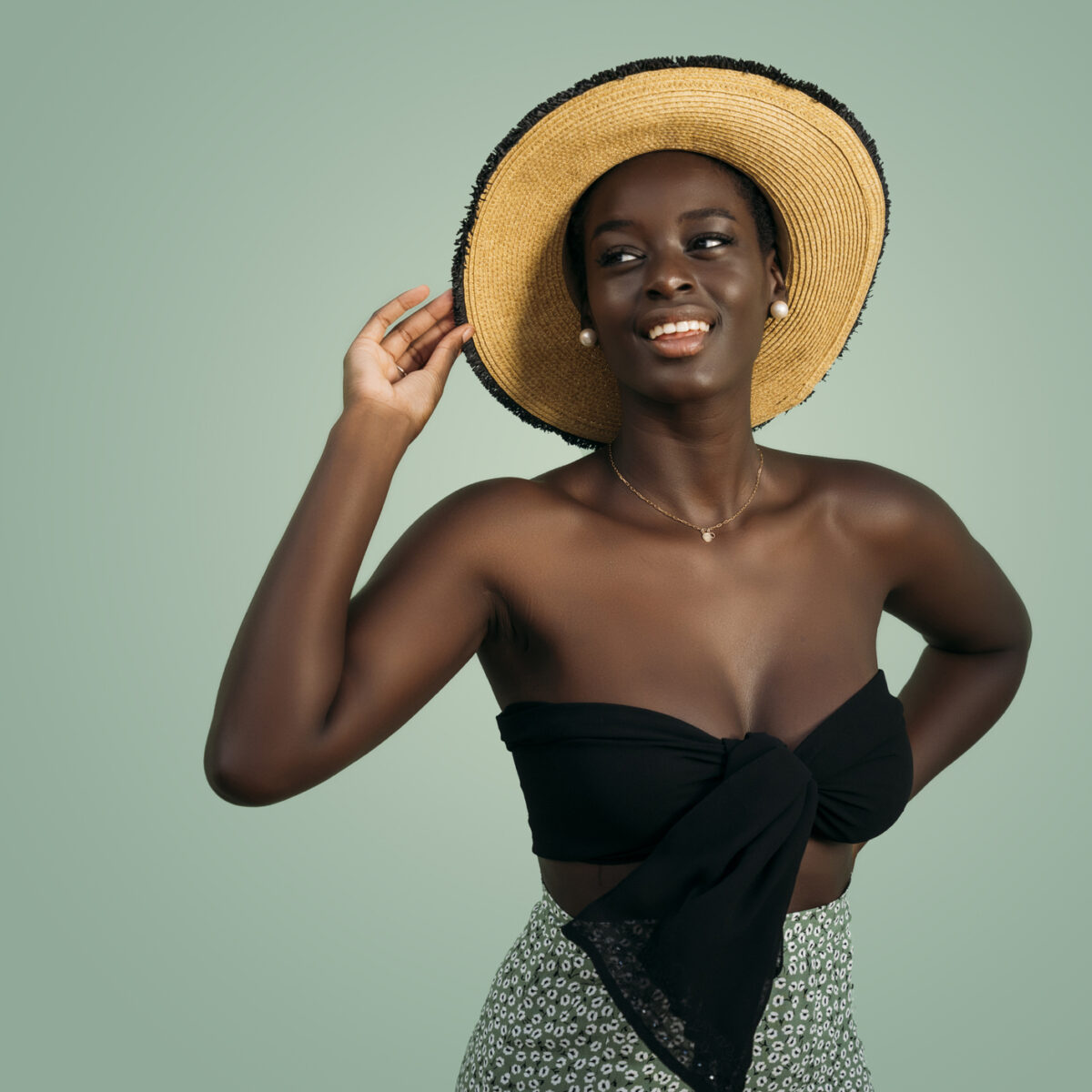 Young adult woman smiling, looking away, and posing with hand on straw hat