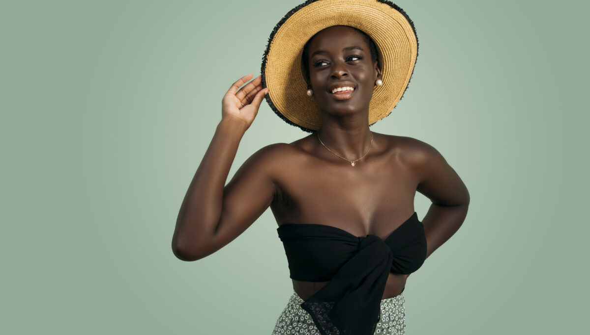 Young adult woman smiling, looking away, and posing with hand on straw hat