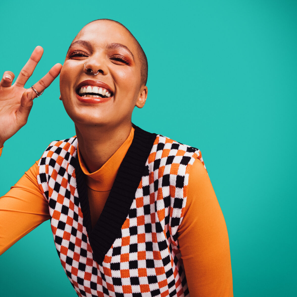 Energy, energetic Happy young woman smiling at the camera., peace sign, while standing alone against a turquoise background.