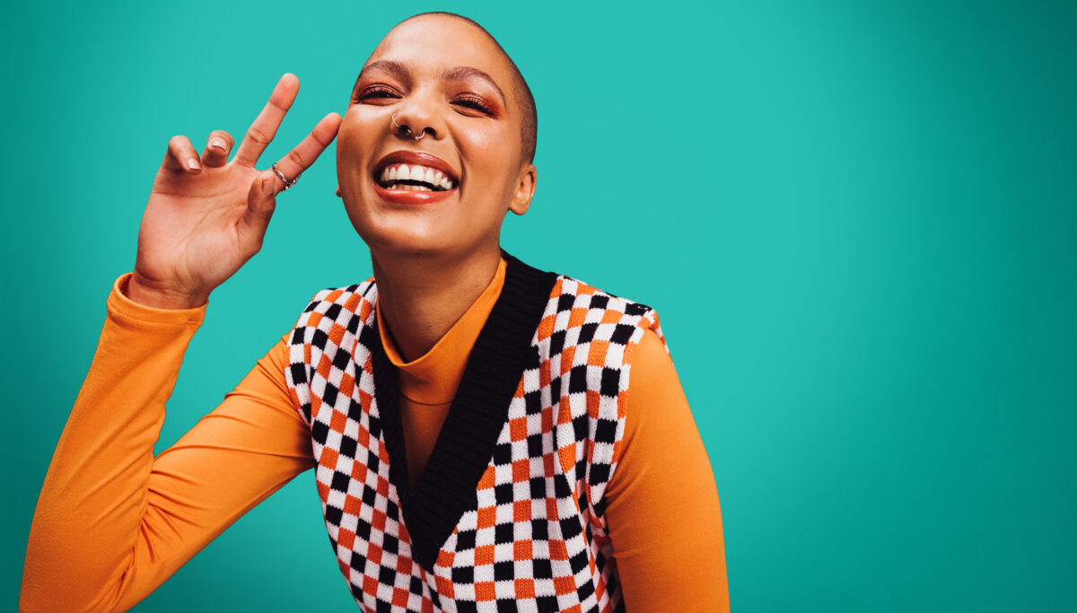 Energy, energetic Happy young woman smiling at the camera., peace sign, while standing alone against a turquoise background.